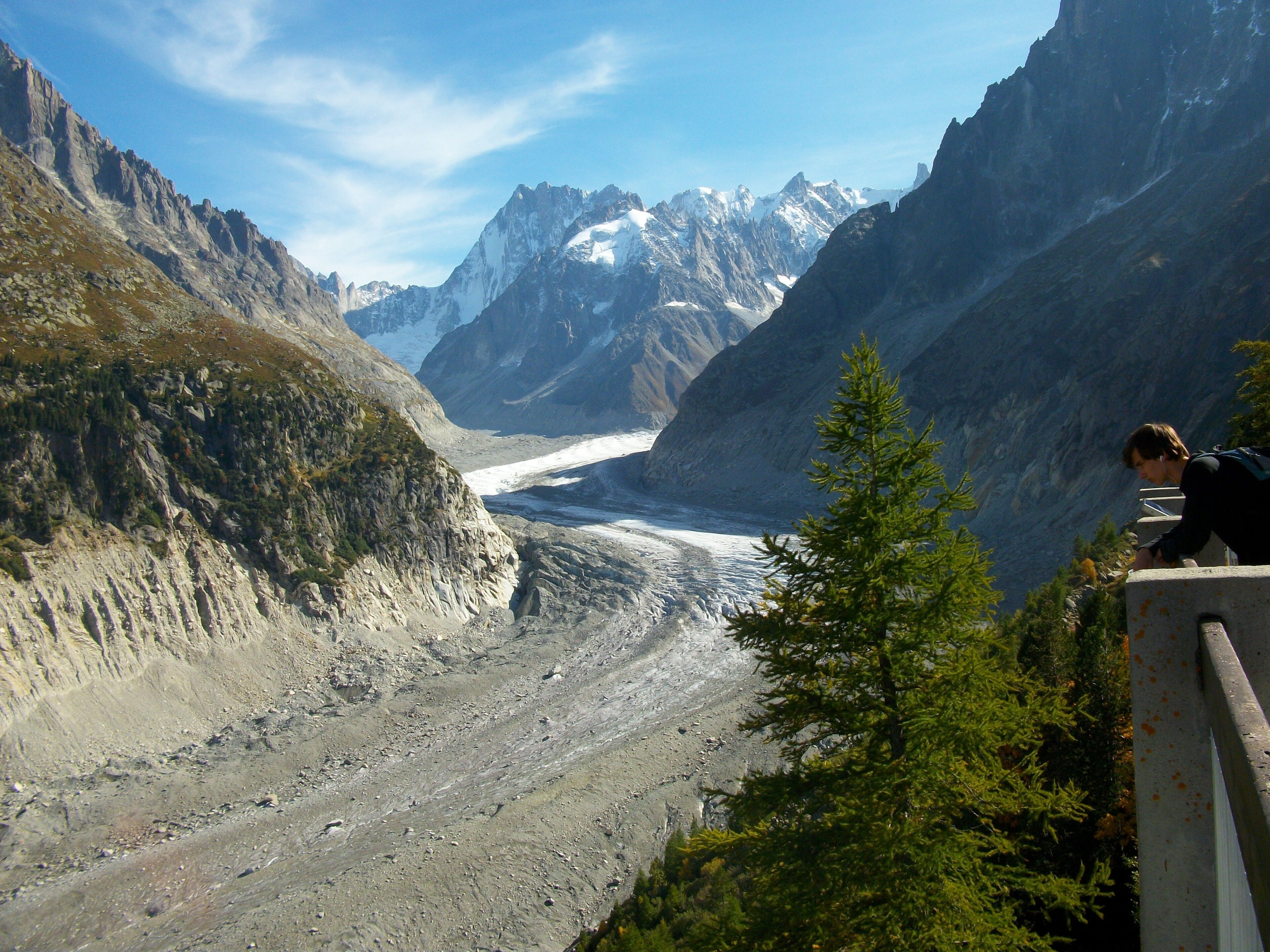 Une vallée glaciaire bordée de montagnes escarpées, et une personne qui contemple le paysage.