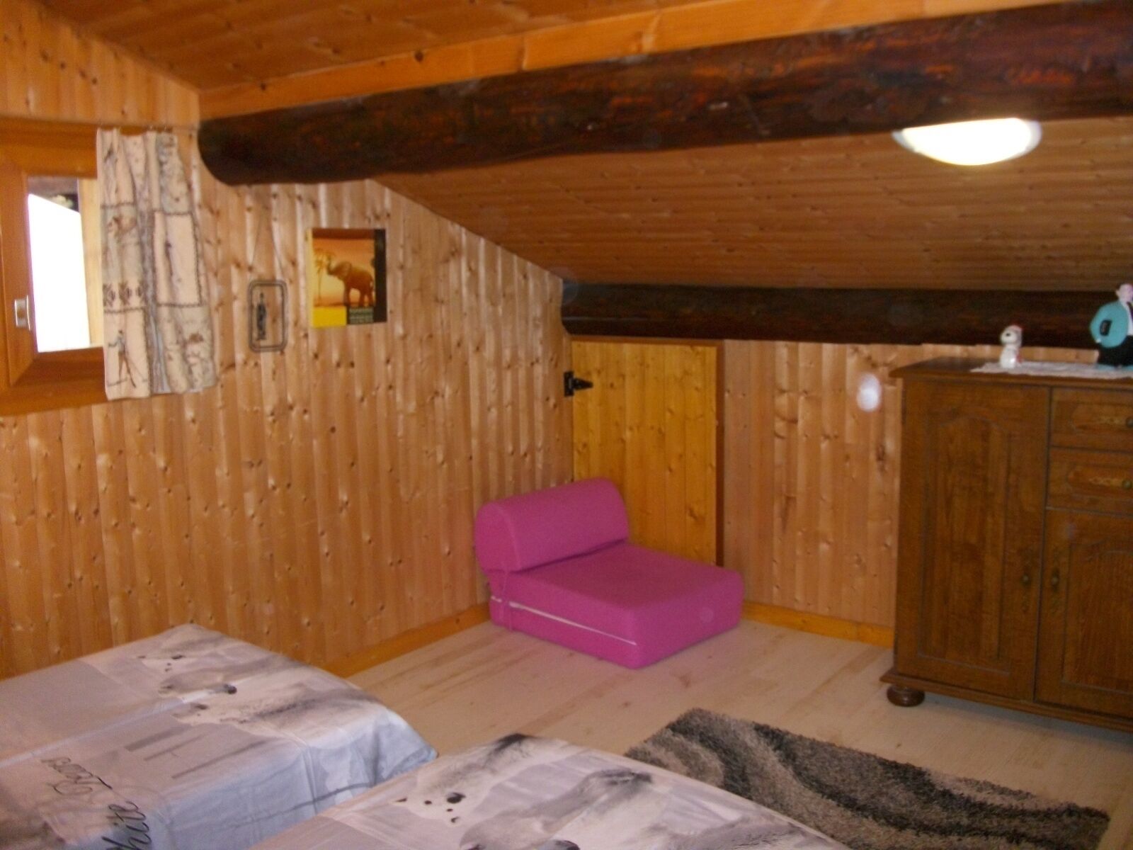 Une pièce de cabane en bois avec deux lits, une chaise rose, un meuble en bois et une petite fenêtre.