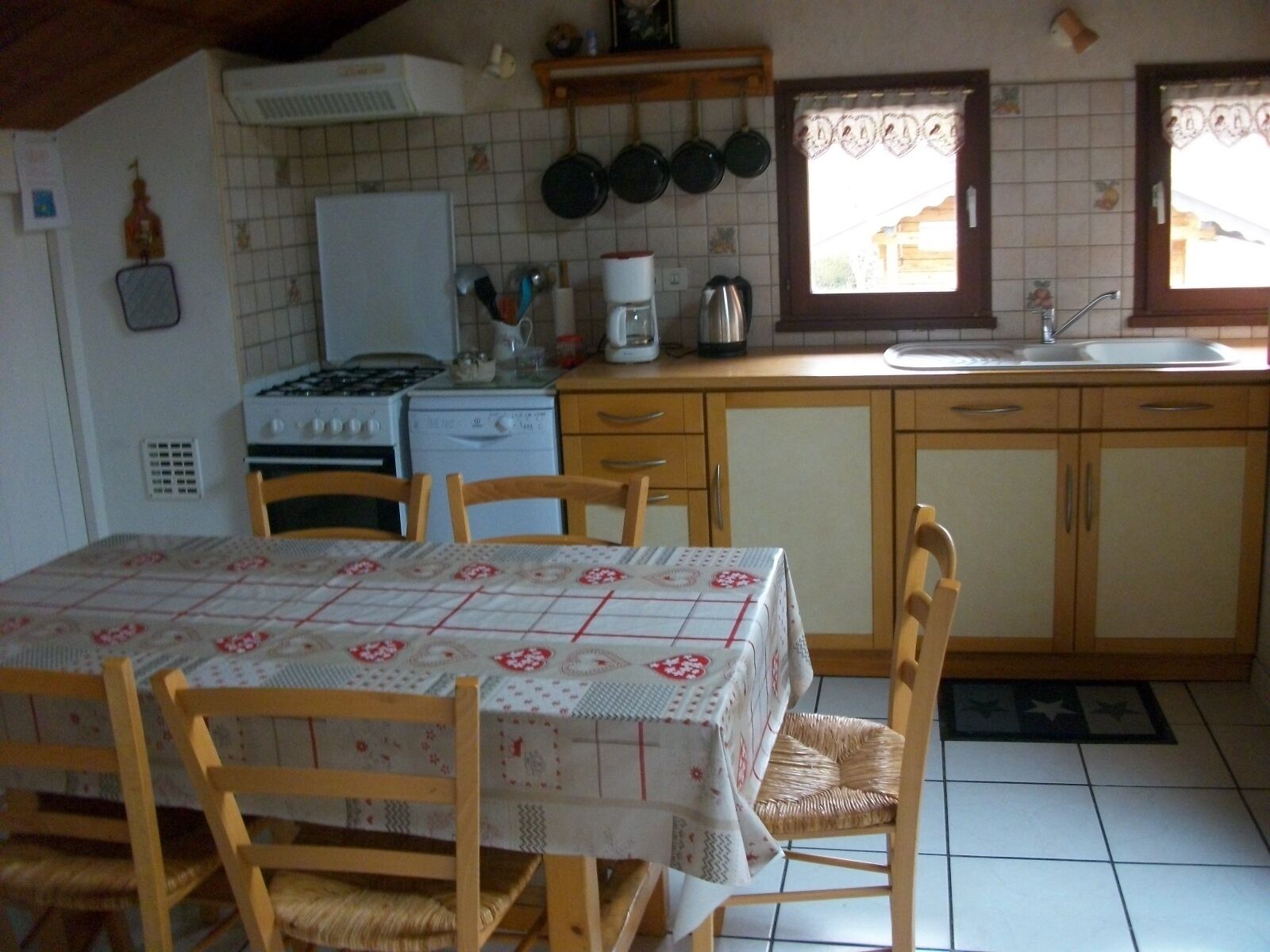 A kitchen with a dining table, chairs, a stove, a sink, and hanging pots.