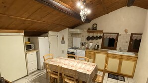 A kitchen with wooden beams, a tiled floor, a dining table with chairs, a refrigerator, a stove, and a sink.