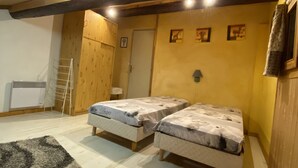 A cozy room with two beds, a wooden ceiling, a radiator, and a door.