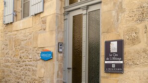 A stone building with a grey door and window shutters. There are two signs: one blue sign with 'Célacacares' and another black sign with 'Le Clos de l'Abbaye' and a QR code. - LE CLOS DE L'ABBAYE 4 * in the heart of the Cité Médiale de Sarlat + Free parking (Sarlat-la-Canéda)
