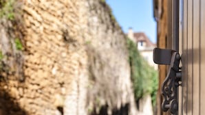 A stone wall with a metal gate, a narrow alley, and a building in the background. - LE CLOS DE L'ABBAYE 4 * in the heart of the Cité Médiale de Sarlat + Free parking (Sarlat-la-Canéda)