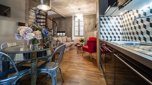 A modern kitchen with a geometric backsplash, a dining area with a glass table and metal chairs, and a staircase leading to an upper level. - LE CLOS DE L'ABBAYE 4 * in the heart of the Cité Médiale de Sarlat + Free parking (Sarlat-la-Canéda)