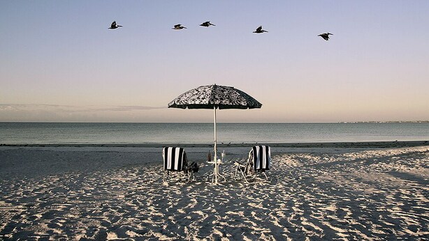 A beach with a single umbrella and two striped beach chairs.