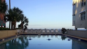 A pool with lounge chairs and palm trees, surrounded by buildings.