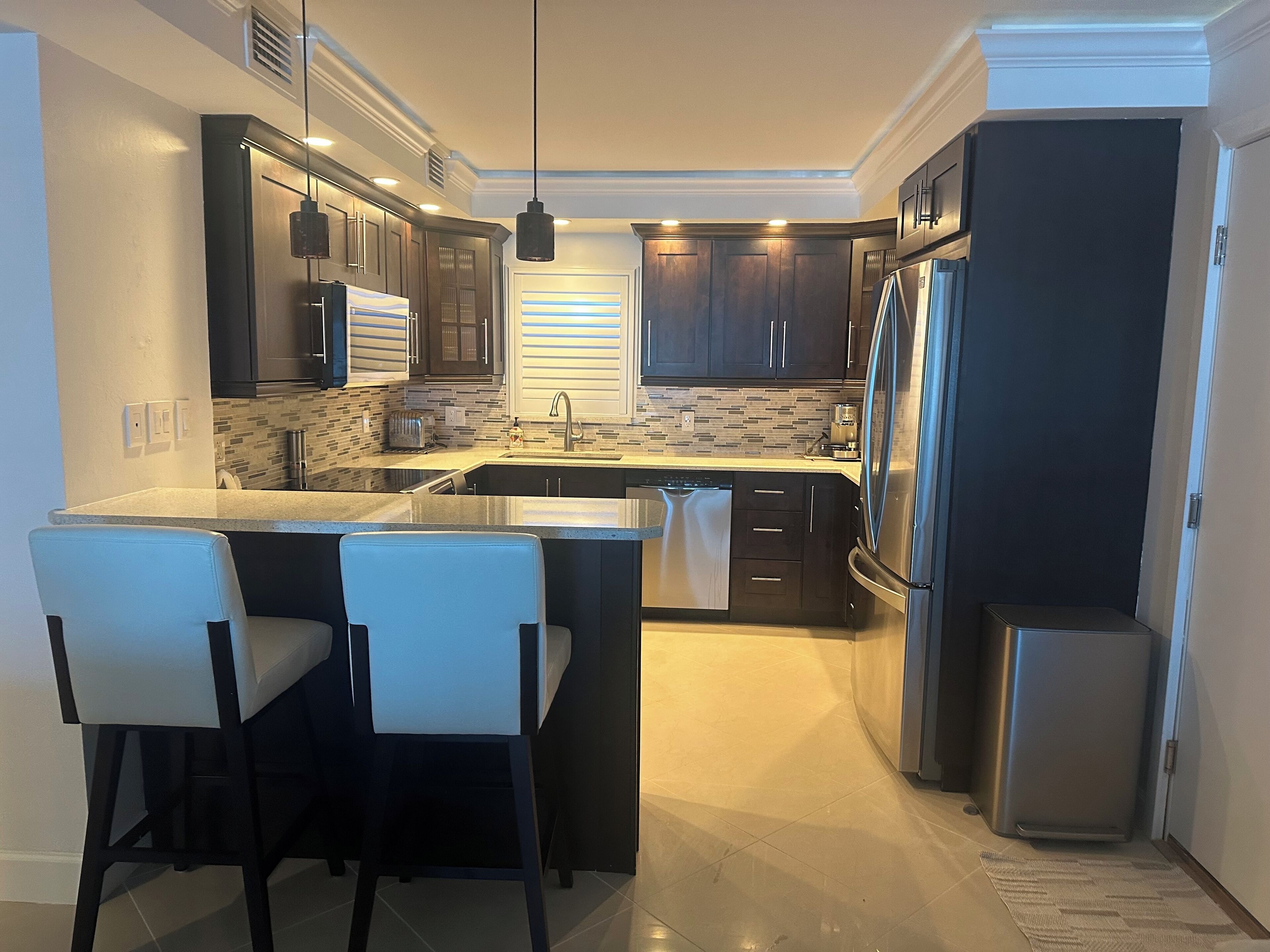 Una cocina moderna con armarios oscuros, un refrigerador de acero inoxidable y una isla central con taburetes de bar.