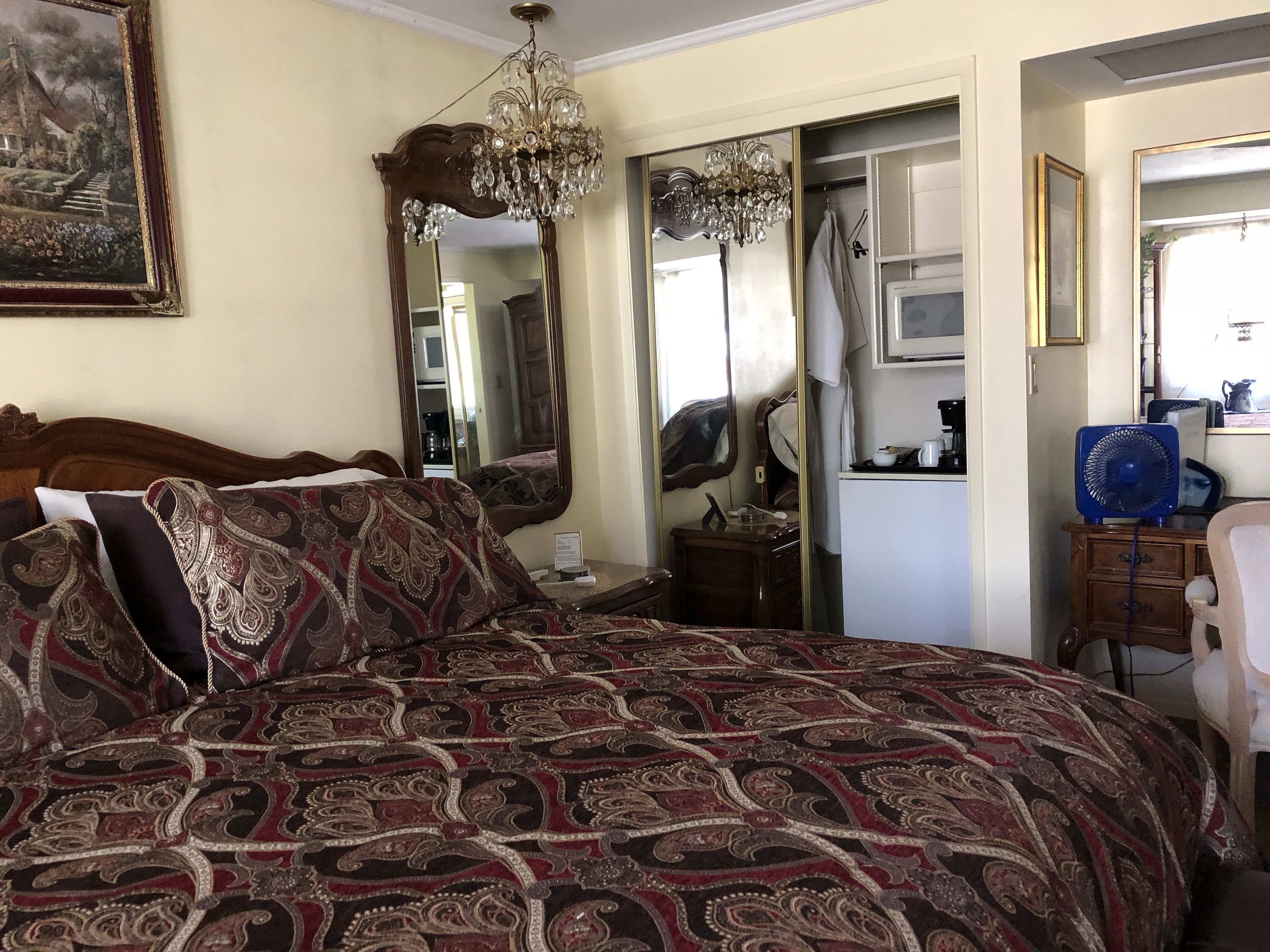 A bedroom with a large bed, a chandelier, a dresser, and a mirror.