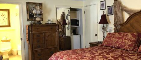 A bedroom with a large bed, a dresser, a mirror, a lamp, and a door leading to a bathroom.