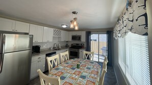 A compact kitchen with white cabinets, a stainless steel refrigerator, a microwave, and a dining table with a colorful tablecloth.
