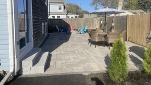 A backyard patio with a table and chairs, a wooden fence, and a small tree.