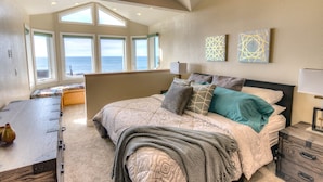 A bedroom with a large bed, a bench at the foot of the bed, and a view of the ocean through large windows. - Amazing Ocean Views in Yachats! Modern Decor! Dog Friendly! (Yachats)