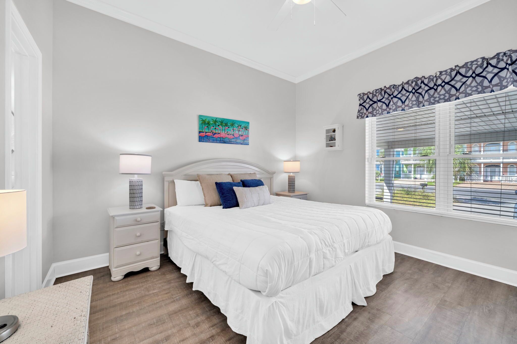 Une chambre à coucher avec un grand lit, deux tables de chevet avec des lampes, une décoration murale et une fenêtre avec des stores.
