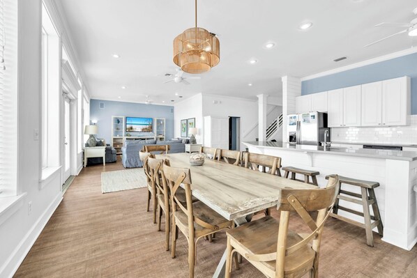 A spacious kitchen with white cabinets, a wooden dining table, and a hanging light fixture.