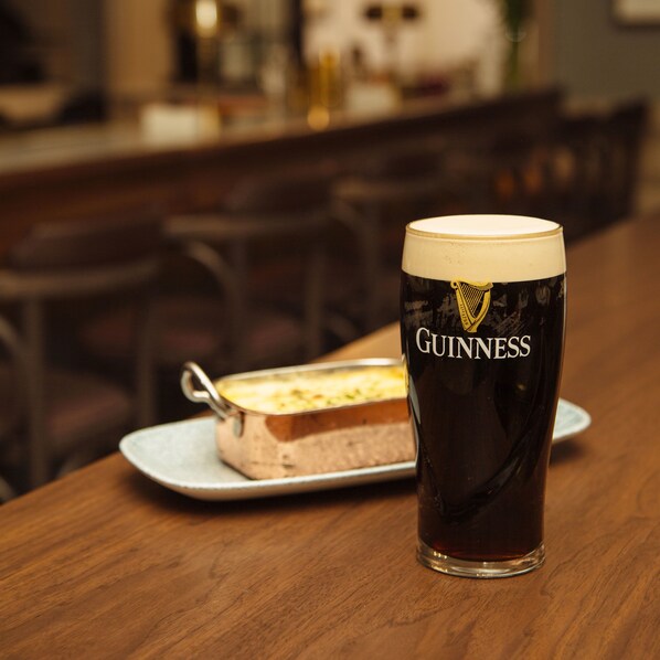 Una cerveza Guinness en un vaso sobre una mesa, con un plato de postre al fondo.