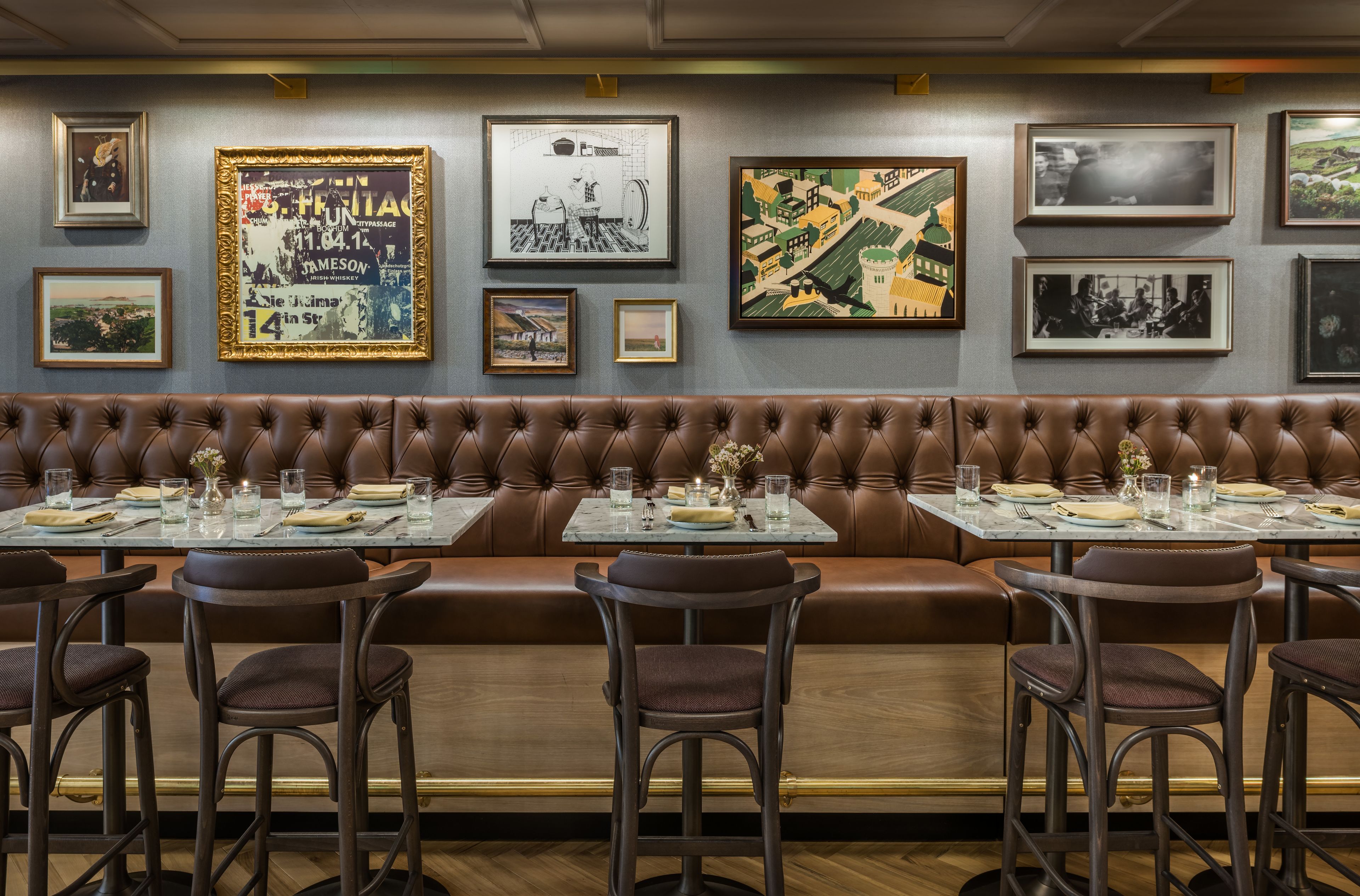 Un ristorante con una zona salotto in pelle marrone, tavoli con sedie e opere d'arte incorniciate alle pareti.