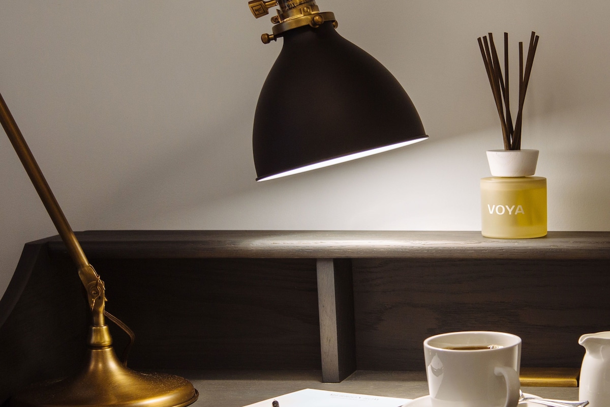 A desk with a brass desk lamp, a white notepad, a pen, a white cup with a saucer, and a small white pitcher.
