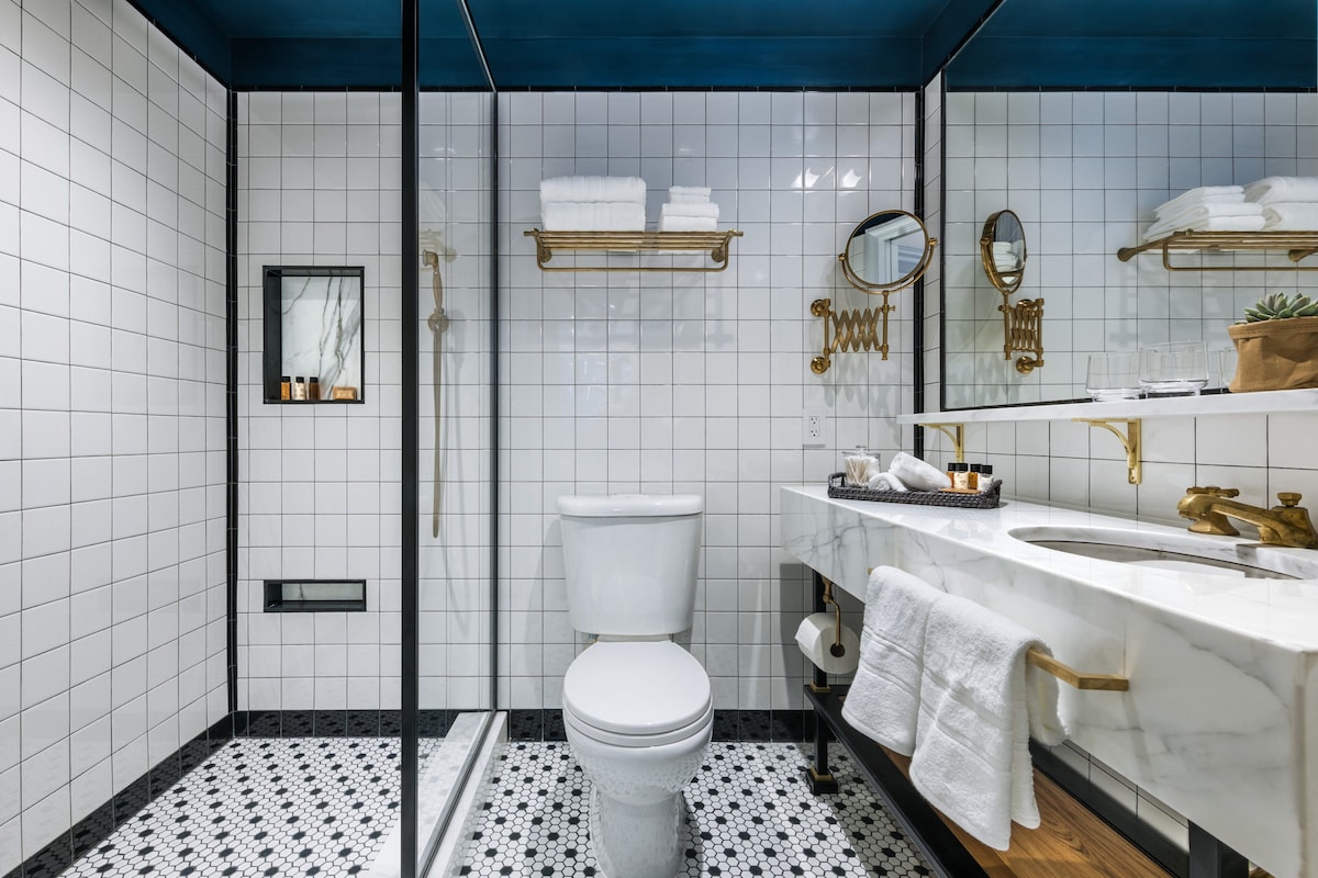 A modern bathroom with a white toilet, a sink with gold fixtures, and a mirror.