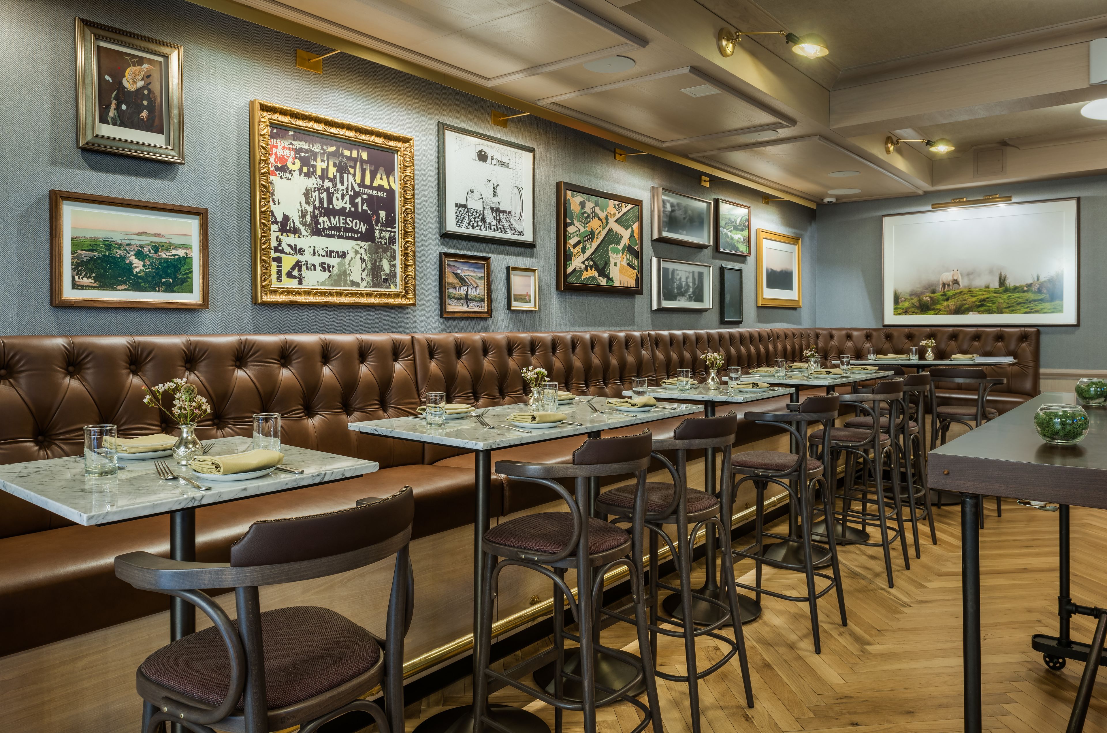 A restaurant with a long brown leather booth seating area, multiple tables with chairs, and framed artwork on the walls.