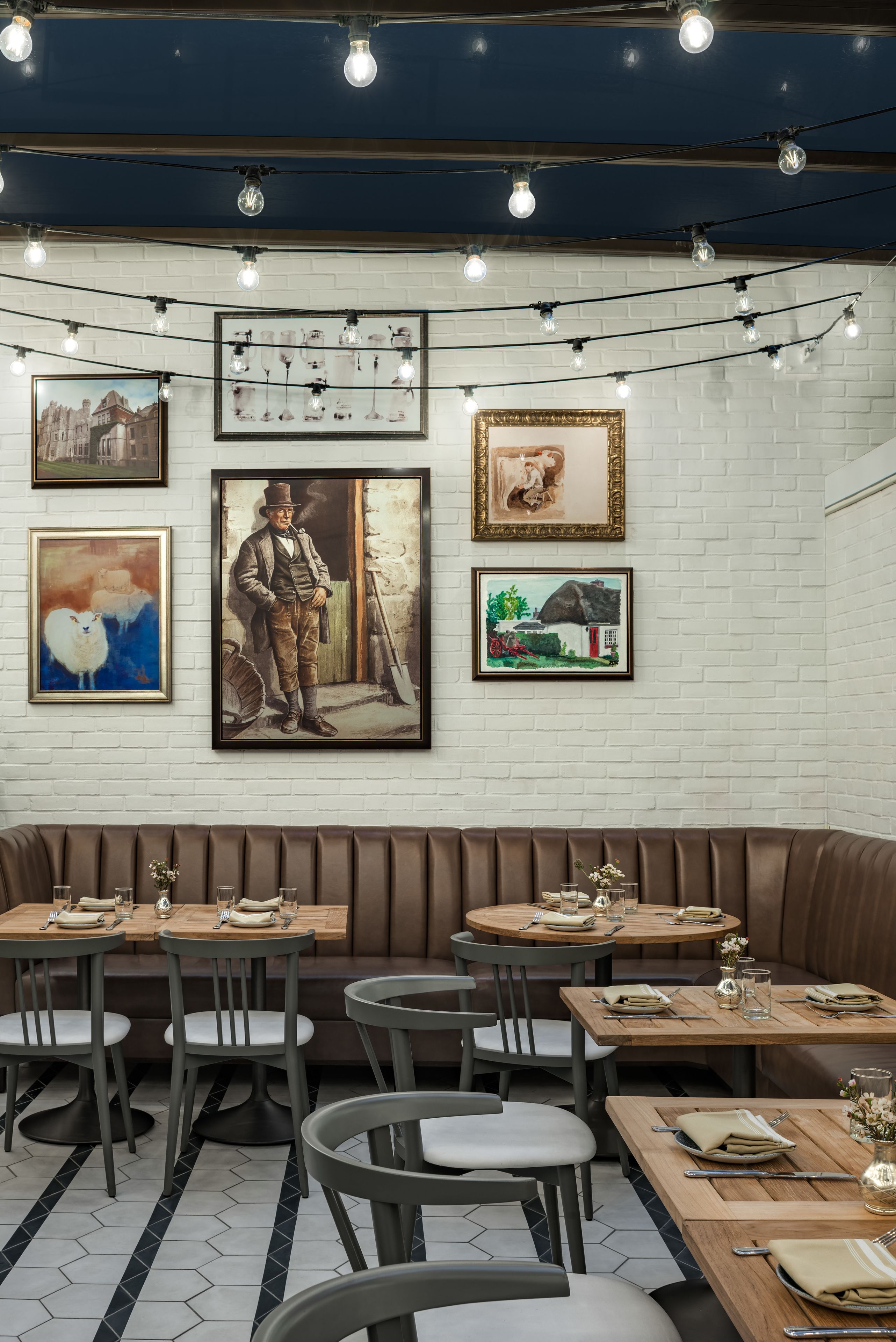 A restaurant with a brick wall, wooden tables, and chairs. There are framed pictures on the wall.