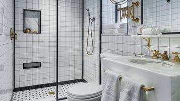 Un baño moderno con inodoro blanco, ducha con cerramiento de vidrio y lavamanos con detalles dorados.
