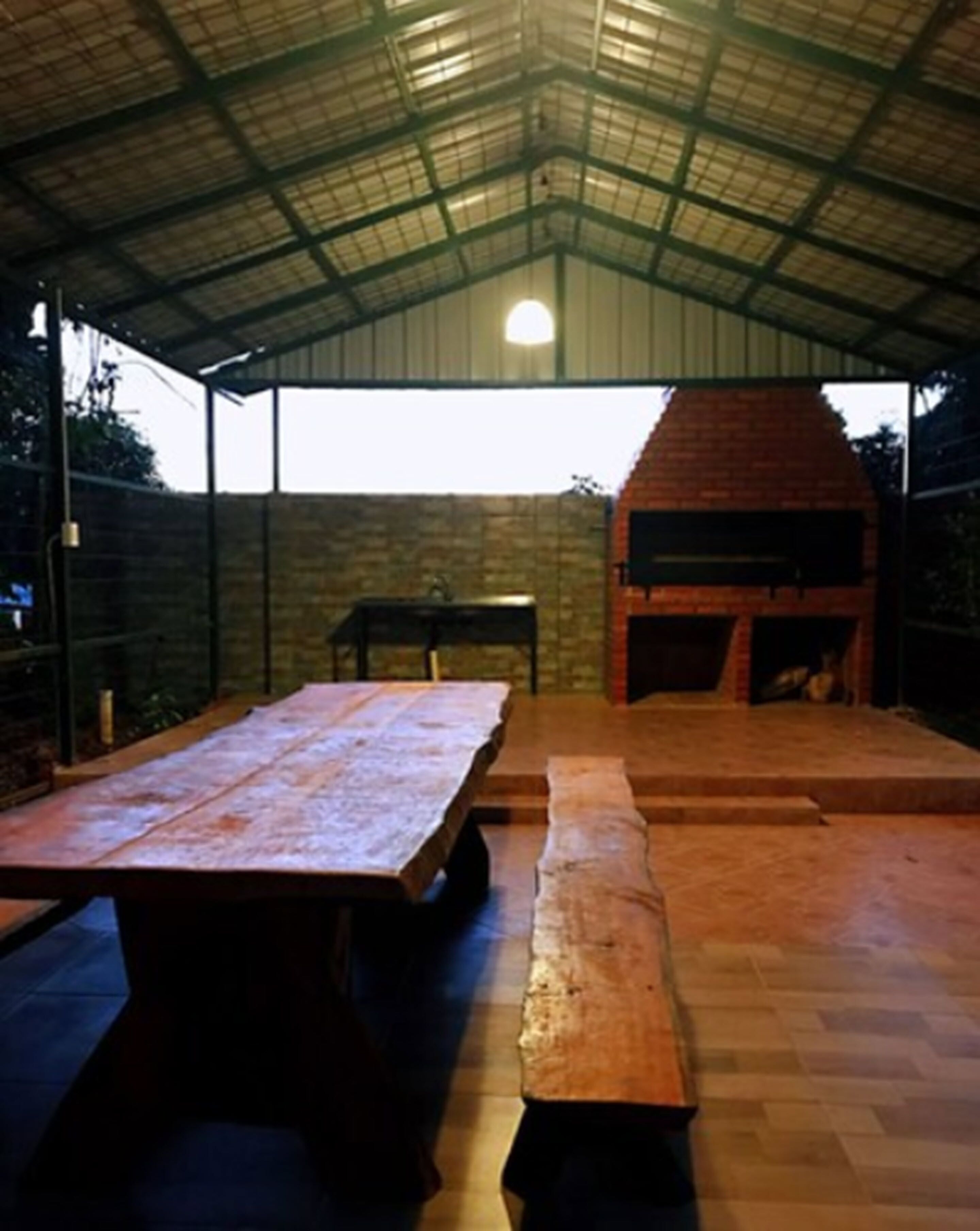 Un patio exterior con un horno de ladrillo, una mesa de madera larga y bancos.