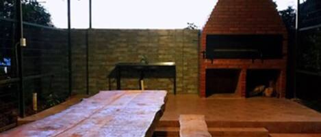 Eine Terrasse im Freien mit einem Backofen aus Ziegelsteinen, einem langen Holztisch und Bänken.