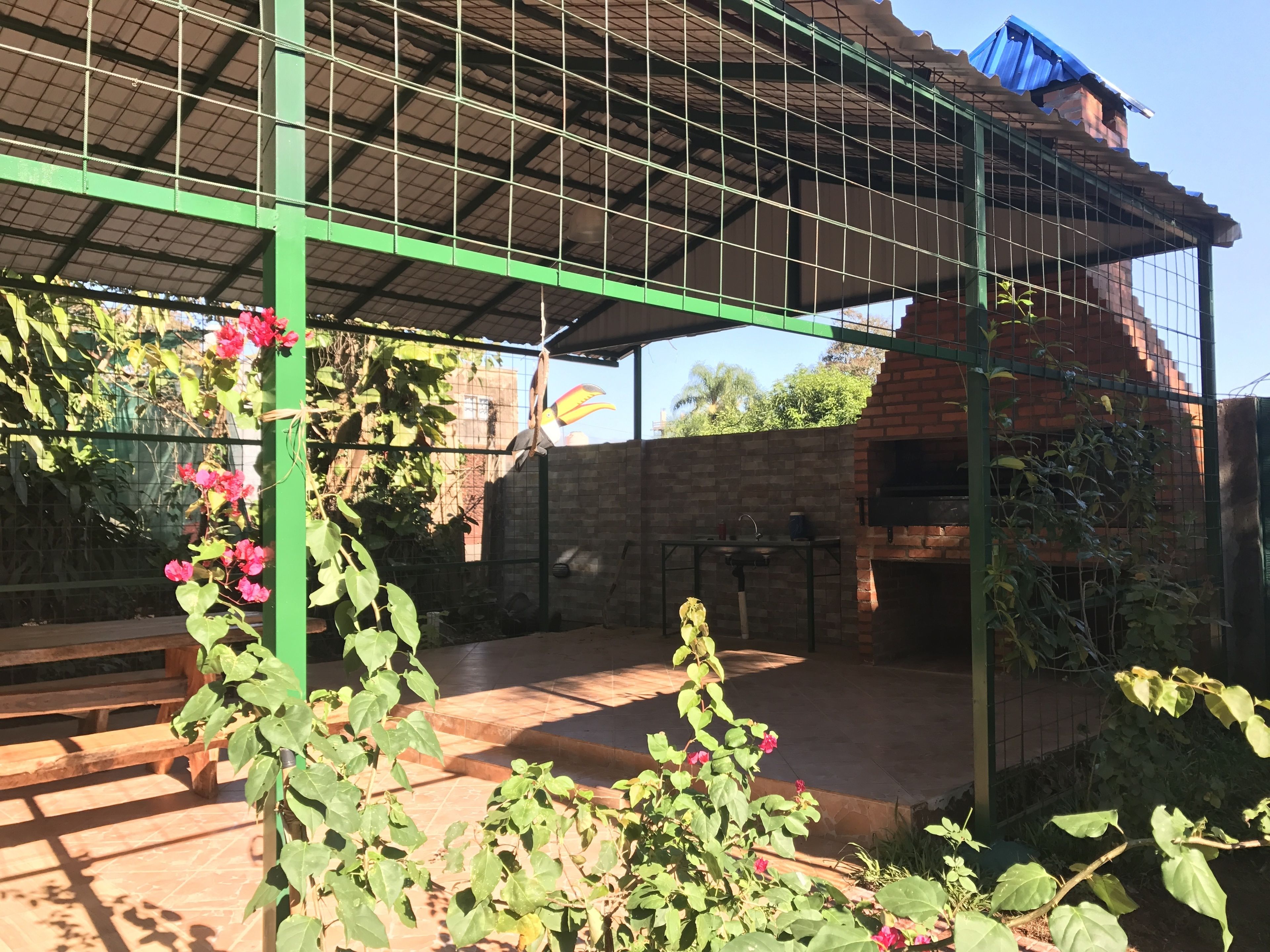 Un patio al aire libre con pared de ladrillo, una parrilla y una pérgola de metal verde.