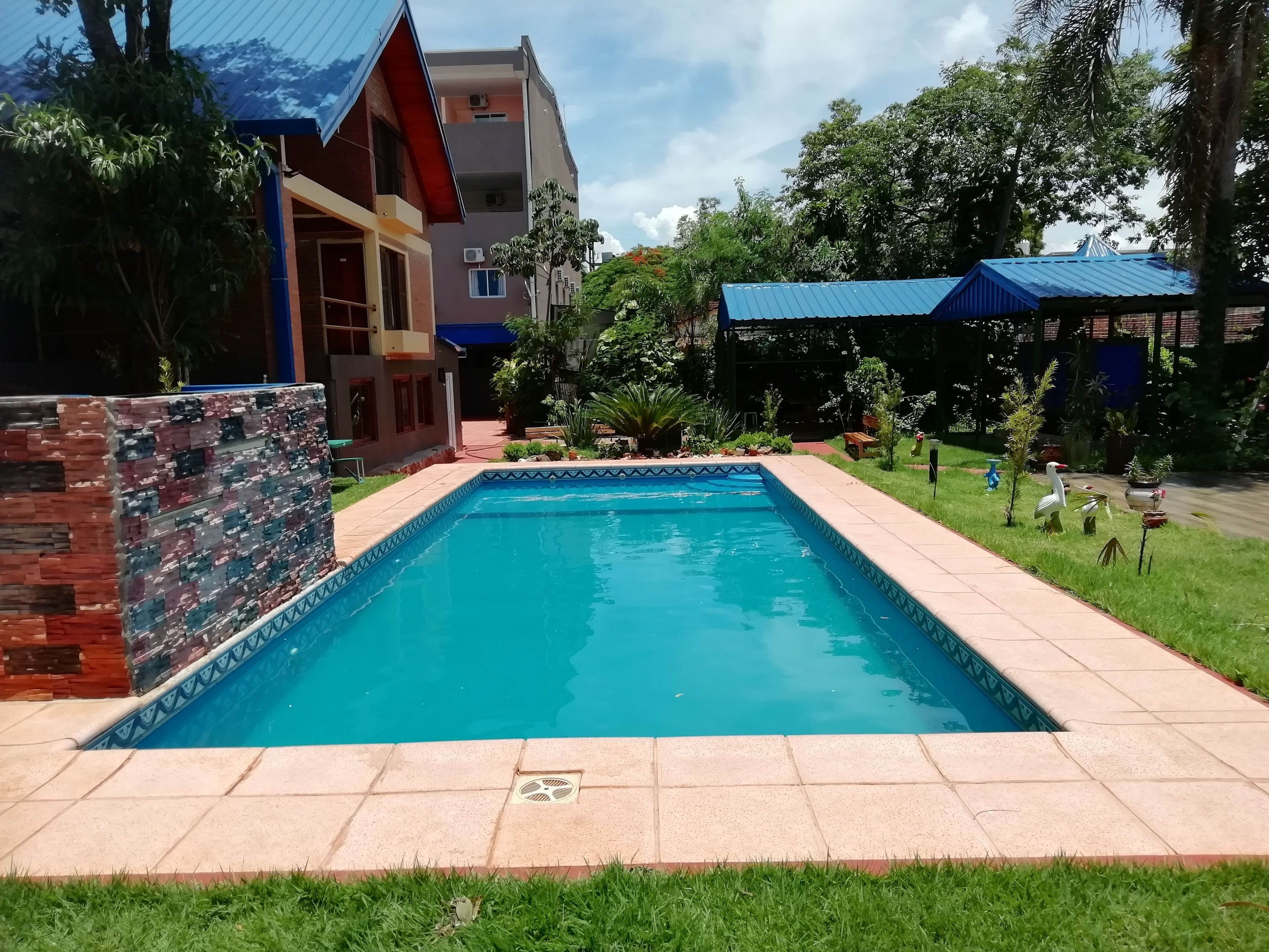 A rectangular swimming pool with a tiled edge, surrounded by a grassy area and a brick wall.