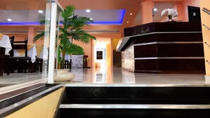 A hotel lobby with a reception desk, a staircase, and a large potted plant. - Hotel Amayal (Puerto Iguazú)