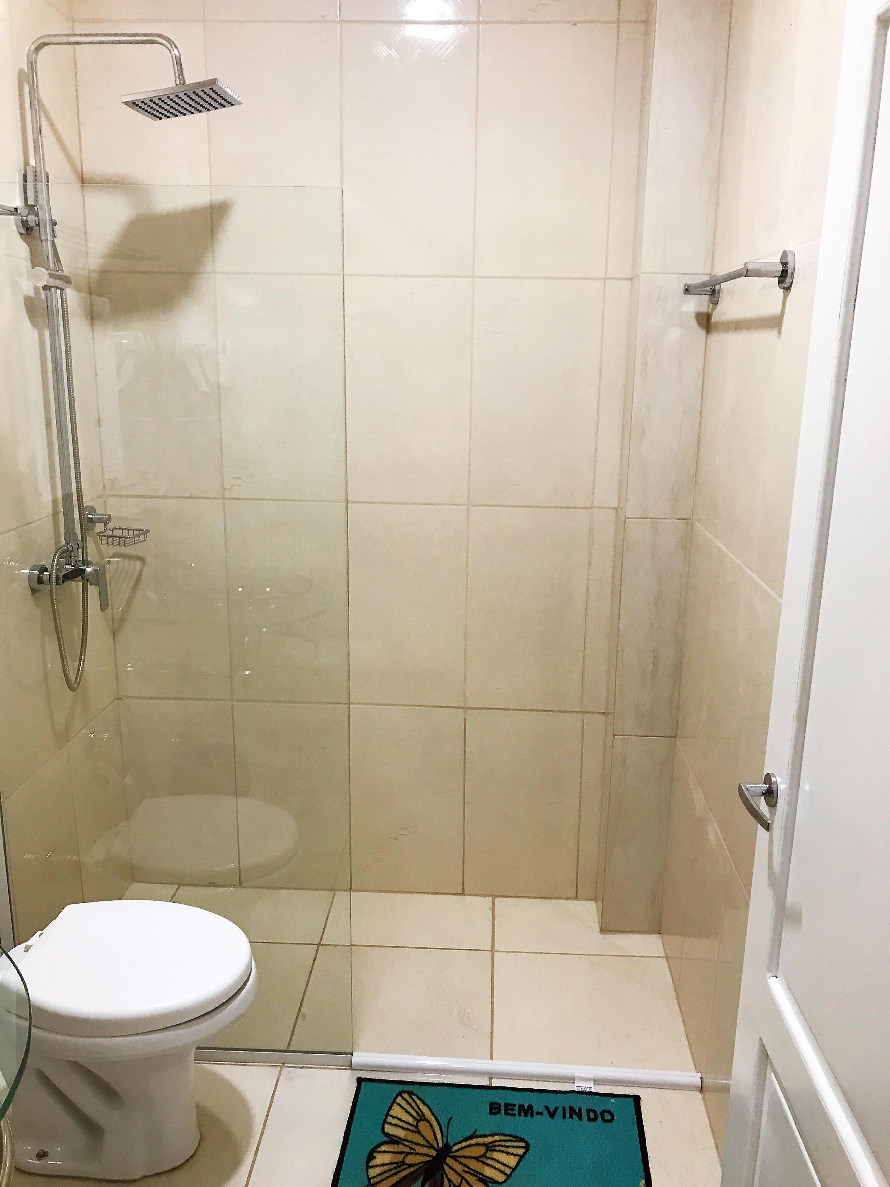 Een kleine betegelde badkamer met een douche, toilet en een deur.