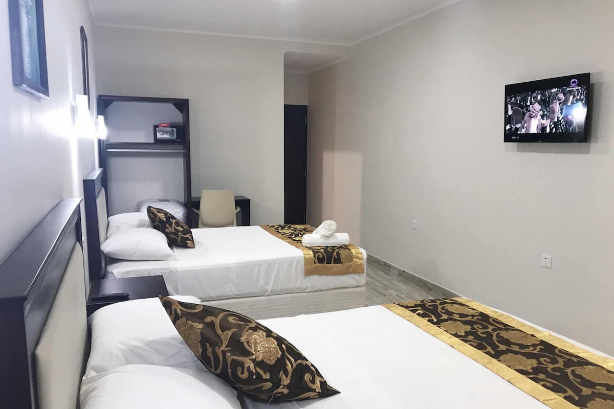 Une chambre d’hôtel avec deux lits, un téléviseur fixé au mur et un bureau avec une chaise.
