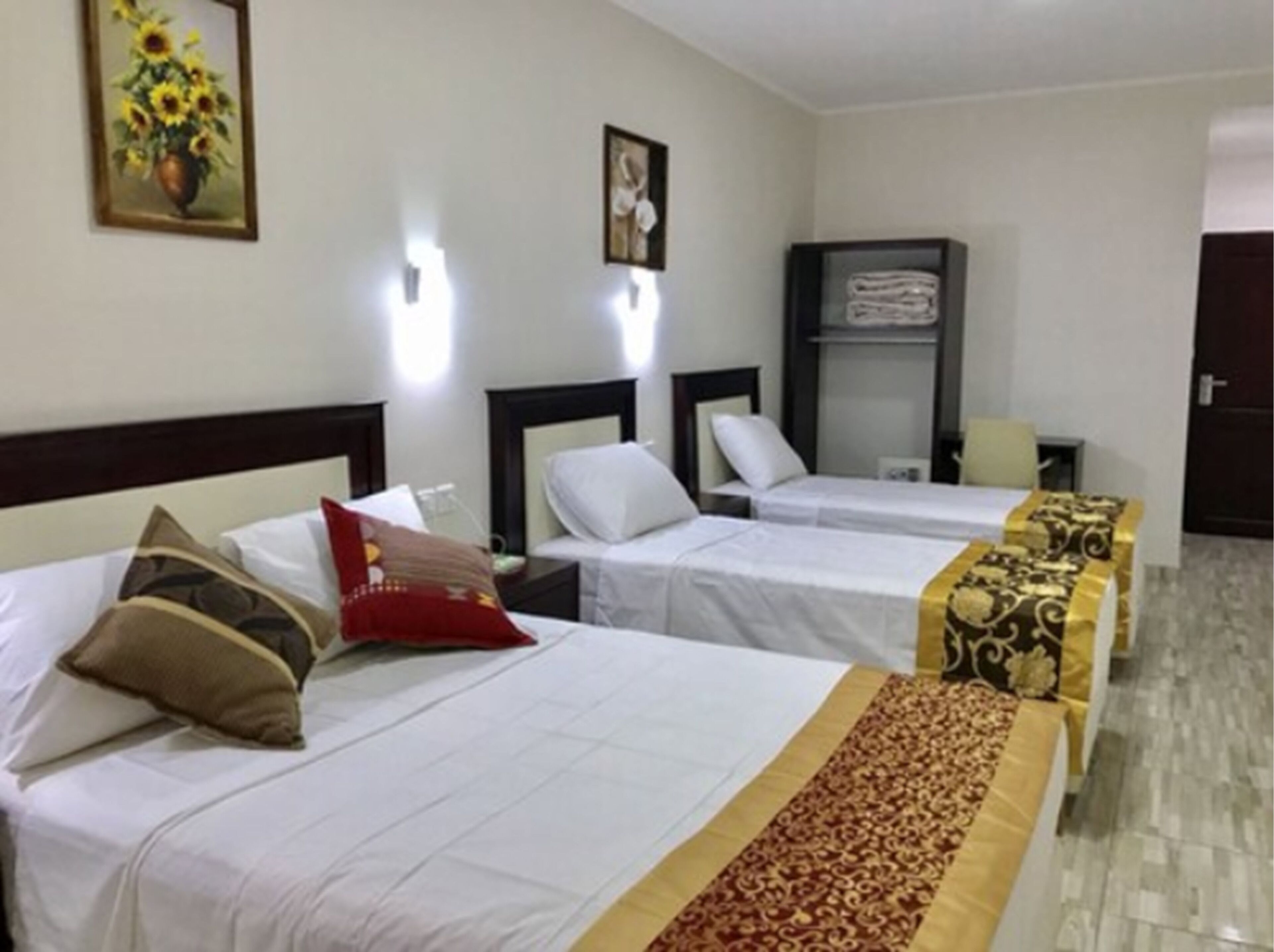 Une chambre d’hôtel avec deux lits simples, une table de chevet, une commode, une armoire et un tableau encadré au mur.