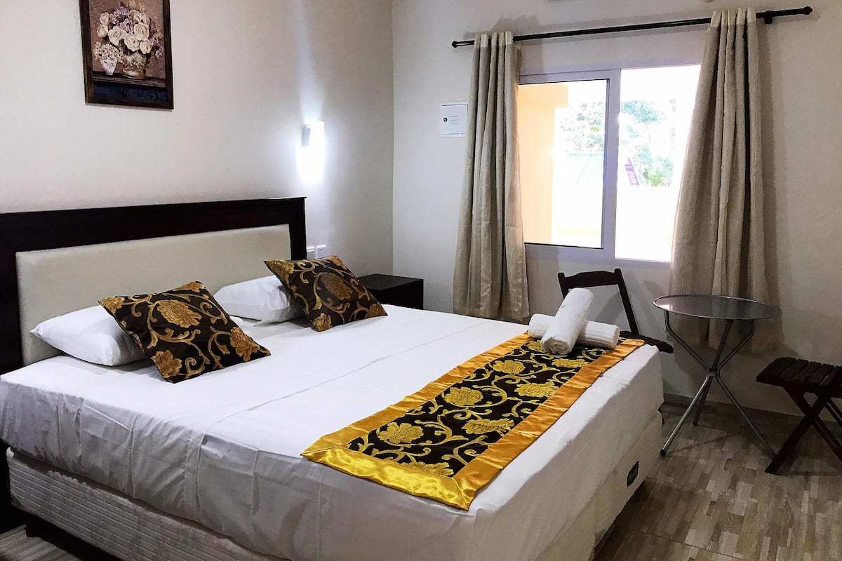 Une chambre d’hôtel comprenant un lit, une table de chevet, une chaise, une fenêtre avec des rideaux et un appareil de climatisation.