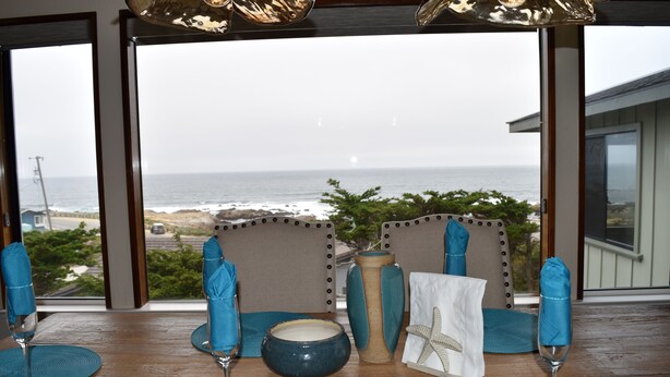 Un espace repas offrant une vue sur l’océan, avec une table dressée agrémentée de serviettes bleues, d’un bol et d’une décoration en forme d’étoile de mer.