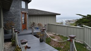 Une maison située sur la côte, avec une façade en pierre, une terrasse en bois et une vue sur l’océan.