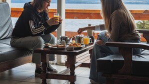 Two people sitting at a wooden table by a large window overlooking a body of water and mountains. - Patagonia Hotel (San Carlos de Bariloche)