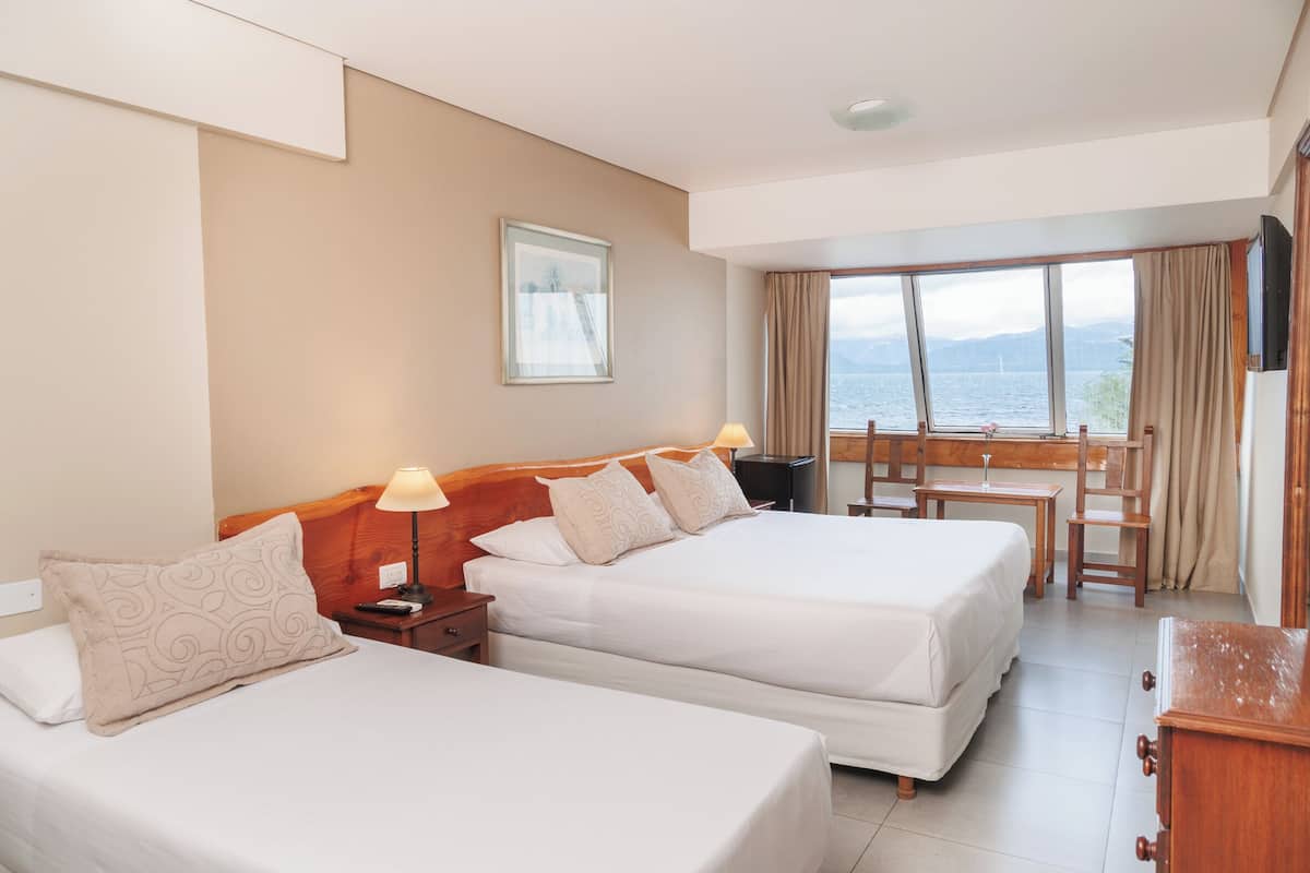 Habitación de hotel con dos camas, un escritorio y vista al mar.