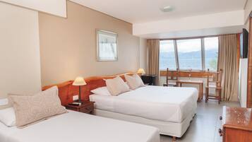 A hotel room with two beds, a desk, and a view of the sea.