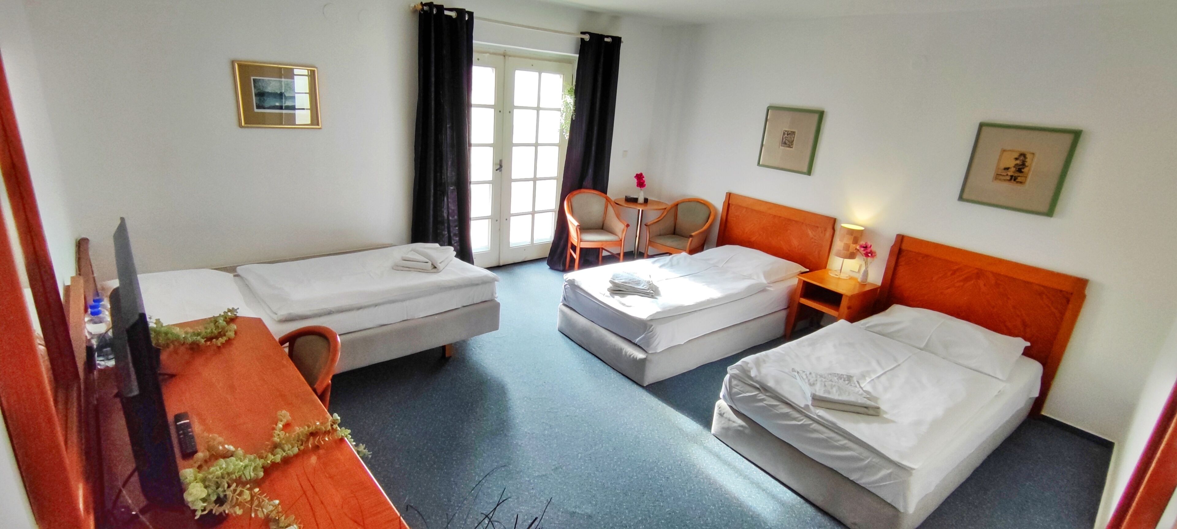 A hotel room with two single beds, a desk with a chair, a small table with a lamp, and a window with curtains.