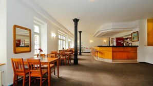 A spacious dining area with wooden tables and chairs, a central column, and a bar area with a Coca-Cola refrigerator. - Hotel Magnolia Roudnice (Roundnice nad Labem)