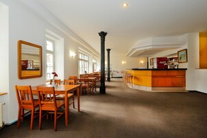 Uma ampla área de refeições com mesas e cadeiras de madeira, uma coluna central e um espaço de bar com refrigerador de Coca-Cola.