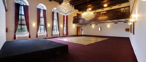 Un amplio salón con techo alto, grandes candelabros y una zona de escenario.