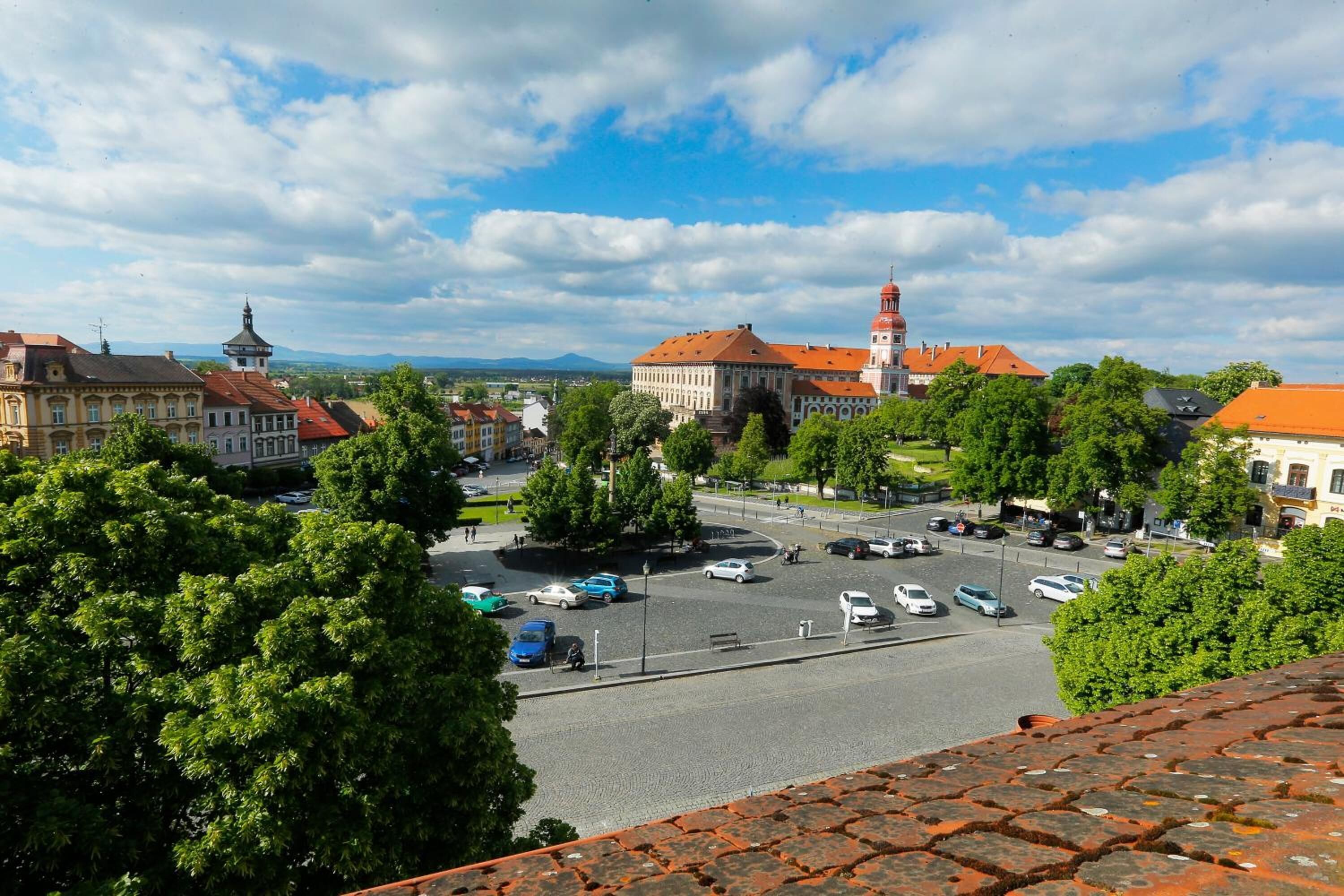 A view of a town square with historic buildings, a prominent tower, and a parking area.