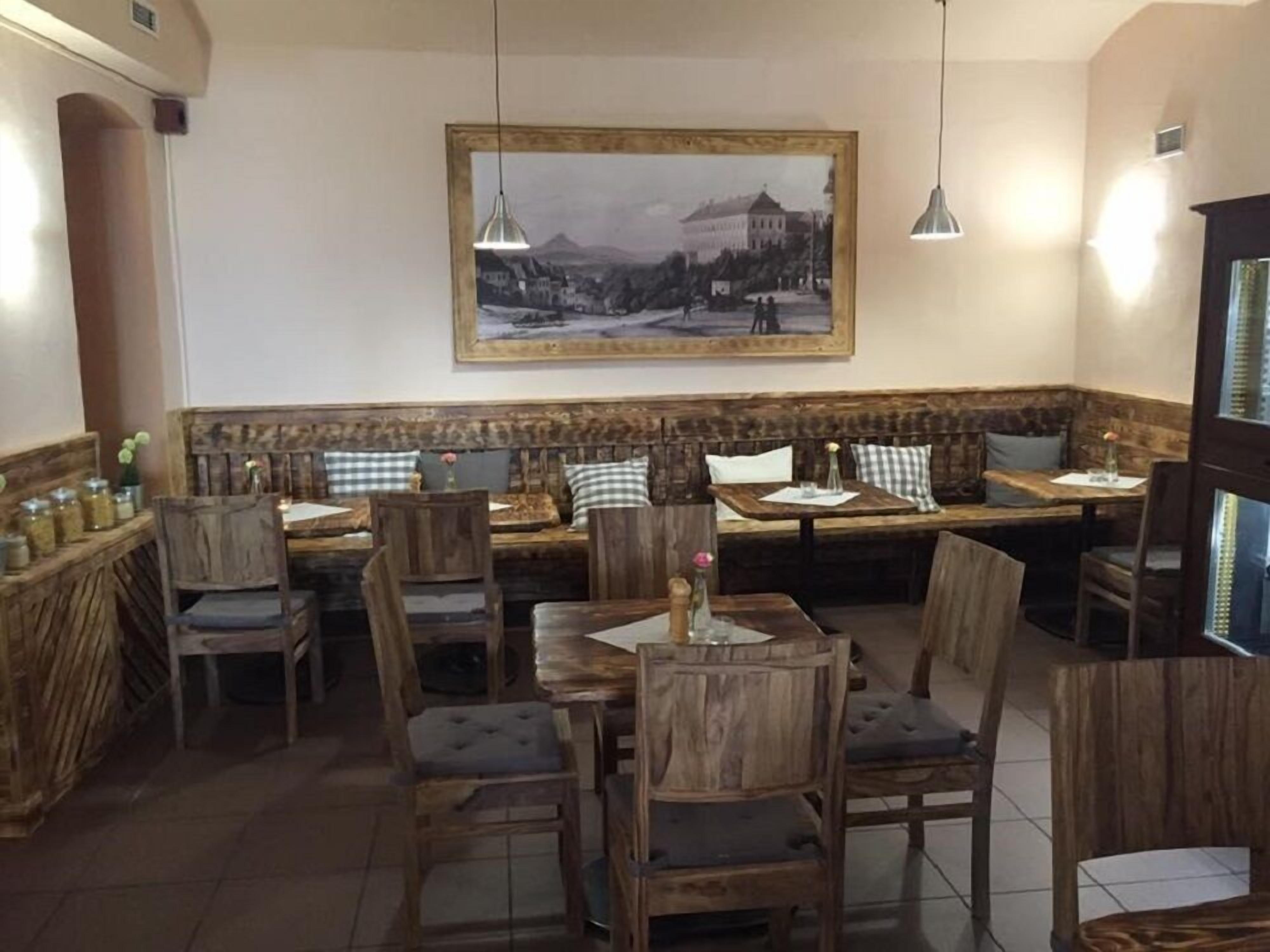 Interior de restaurante con mobiliario de madera, un cuadro grande en la pared y lámparas colgantes.