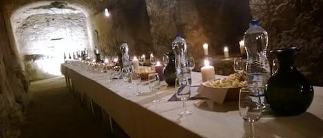 A long table set with glasses, candles, and bottles in a stone-walled room.