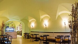 A restaurant with a cozy interior, featuring a counter with a display case, multiple seating areas with tables and chairs, and decorative wall sconces. - Hotel Magnolia Roudnice (Roundnice nad Labem)