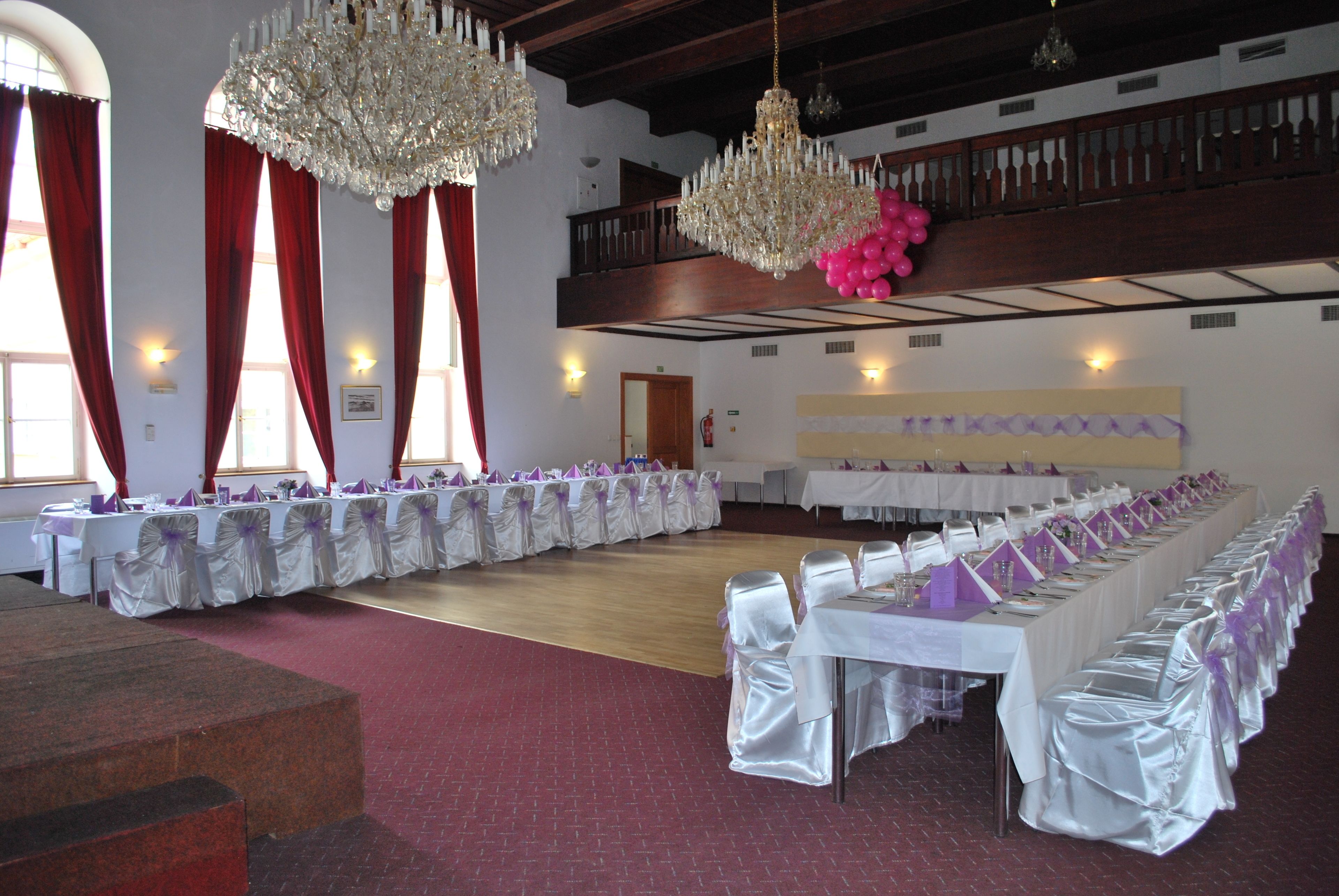 Un salón de banquetes con largas mesas, candelabros y un techo alto.