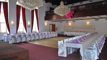 Un salón de banquetes con largas mesas, candelabros y un techo alto.