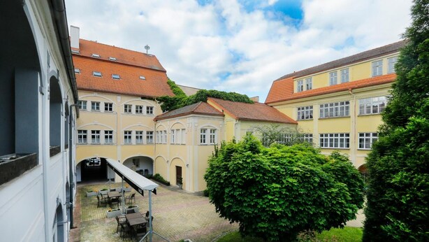 A courtyard with a covered seating area, surrounded by buildings with red-tiled roofs and a central tree. - Hotel Magnolia Roudnice (Roundnice nad Labem)